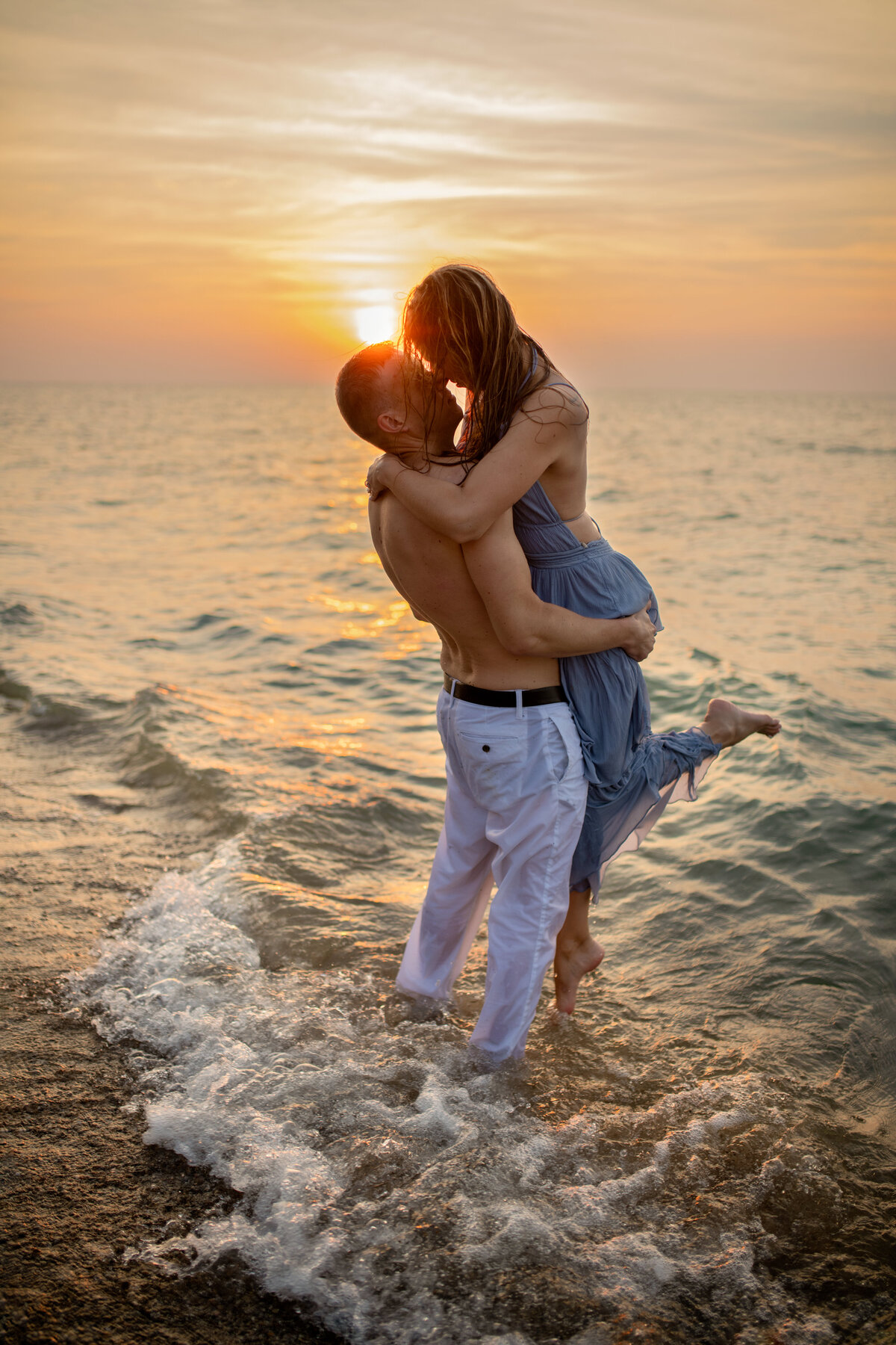 sexy engagement picture of a couple in the  waves at the beach during  golden sunset