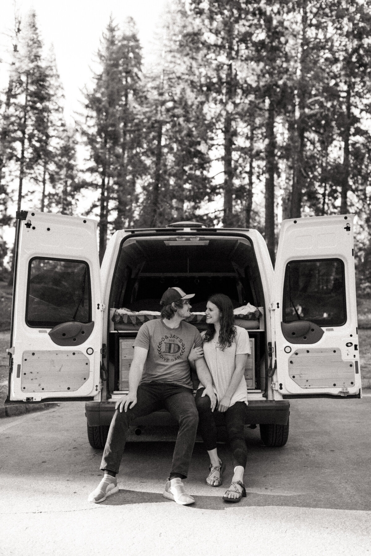 Couple sitting on their camper van in the woods with trees behind them