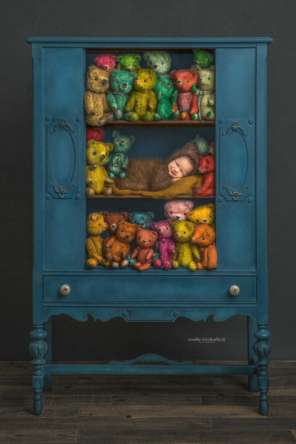 Newborn dressed as a teddy bear snoozing in a blue cupboard full of teddy bears.