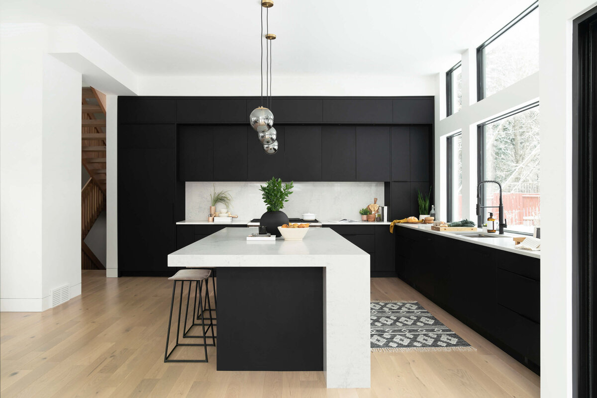 side view of open modern black and white luxury kitchen with wide plank bleached solid wood floors, carrera marble countertop, black luxury cabinetry and pendant lighting