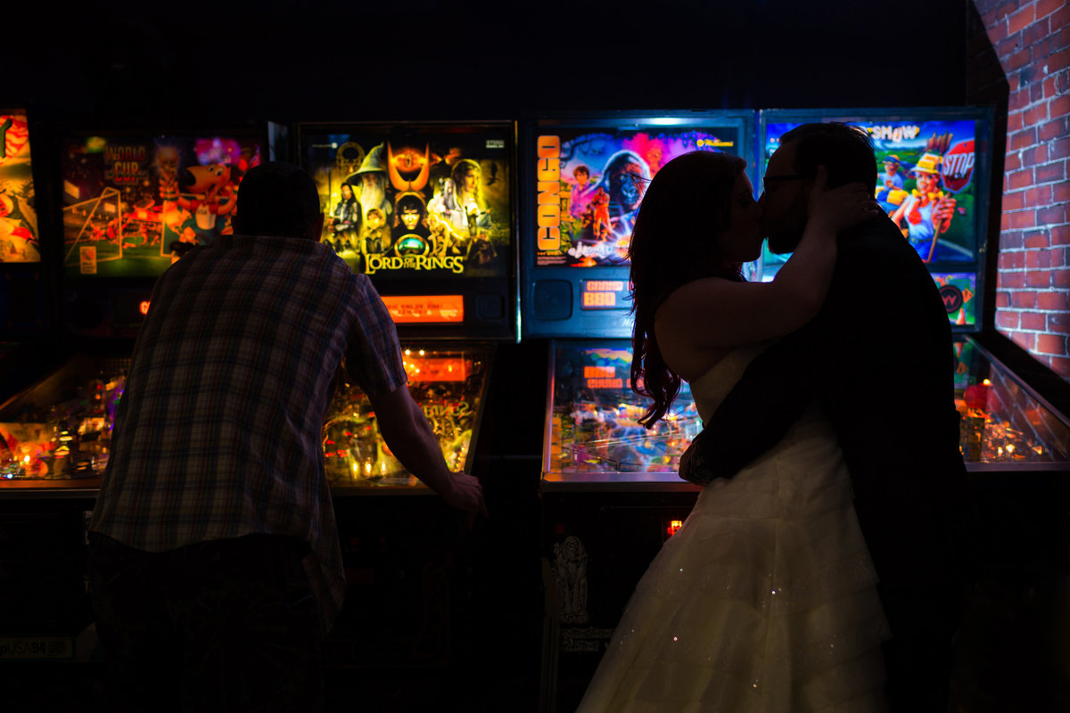 The newlyweds kiss in front of an arcade game at Arcadia in Portland Maine