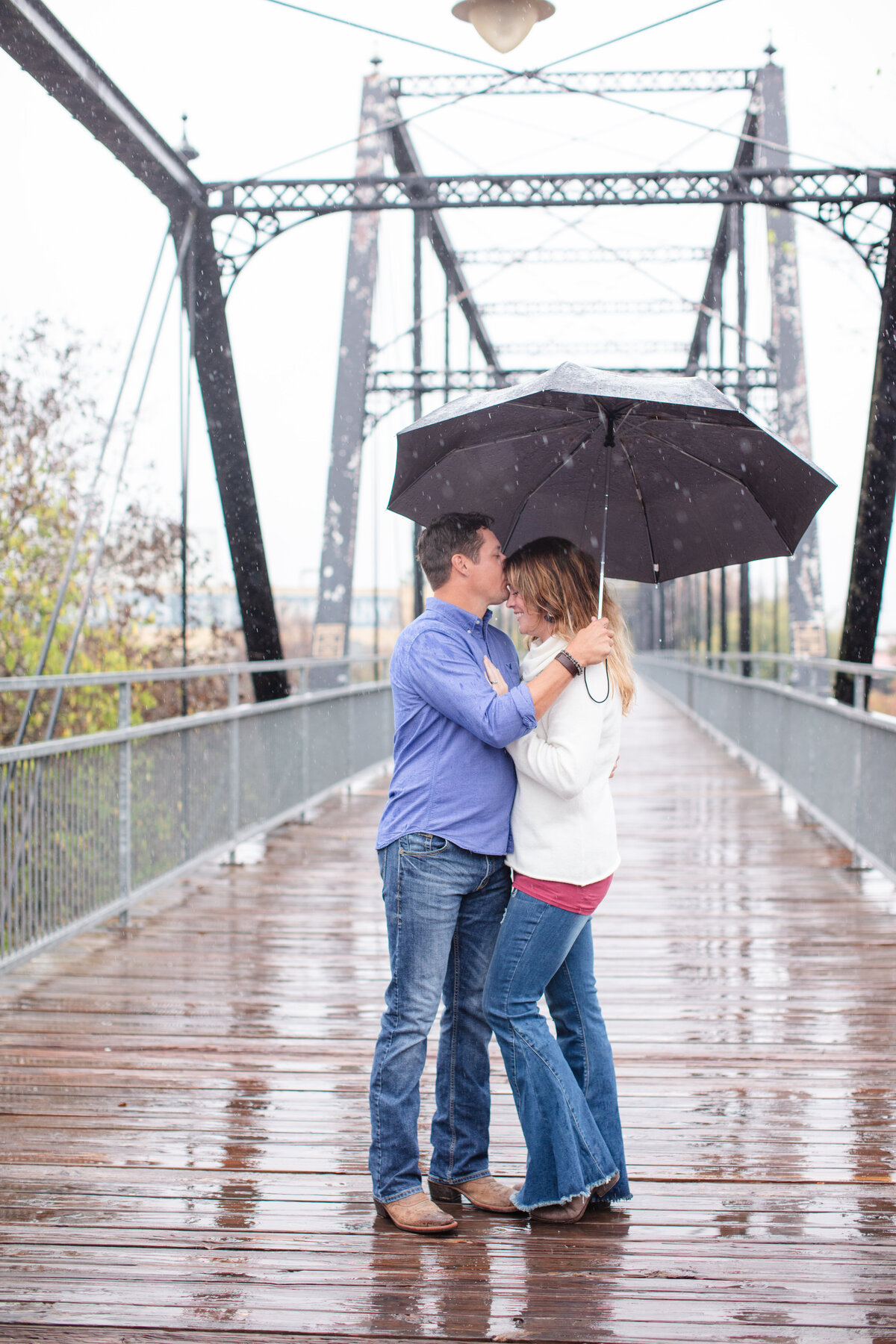 Faust Bridge in New Braunfels Texas couple stands in rain holding umbrella by Firefly Photography