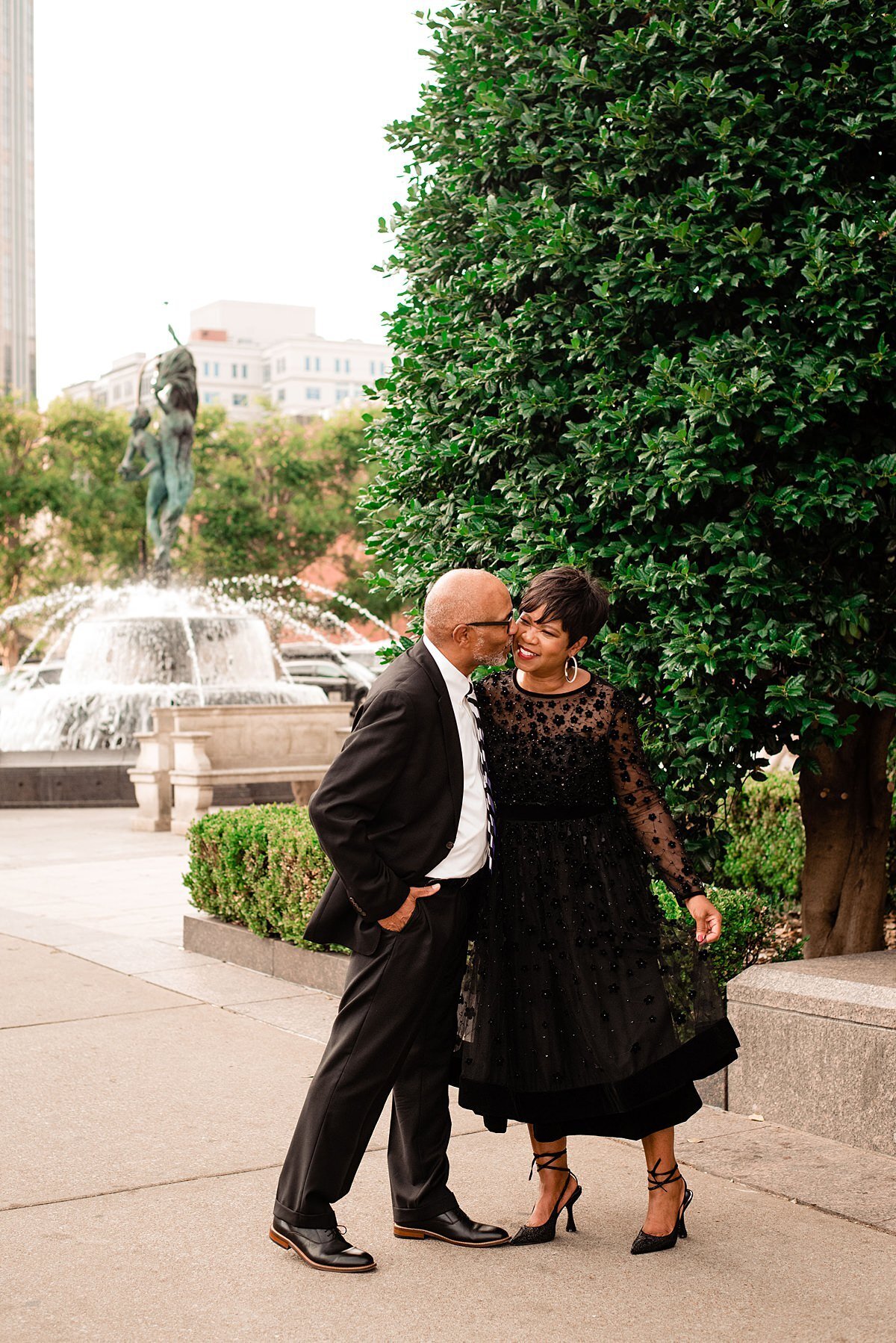 Husband kissing his wife on the cheek outside the symphony center with the fountain behind them