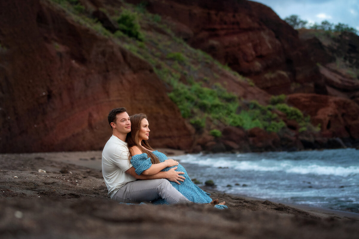 Pregnant couple watching waves at the balck sand beach in Hawaii