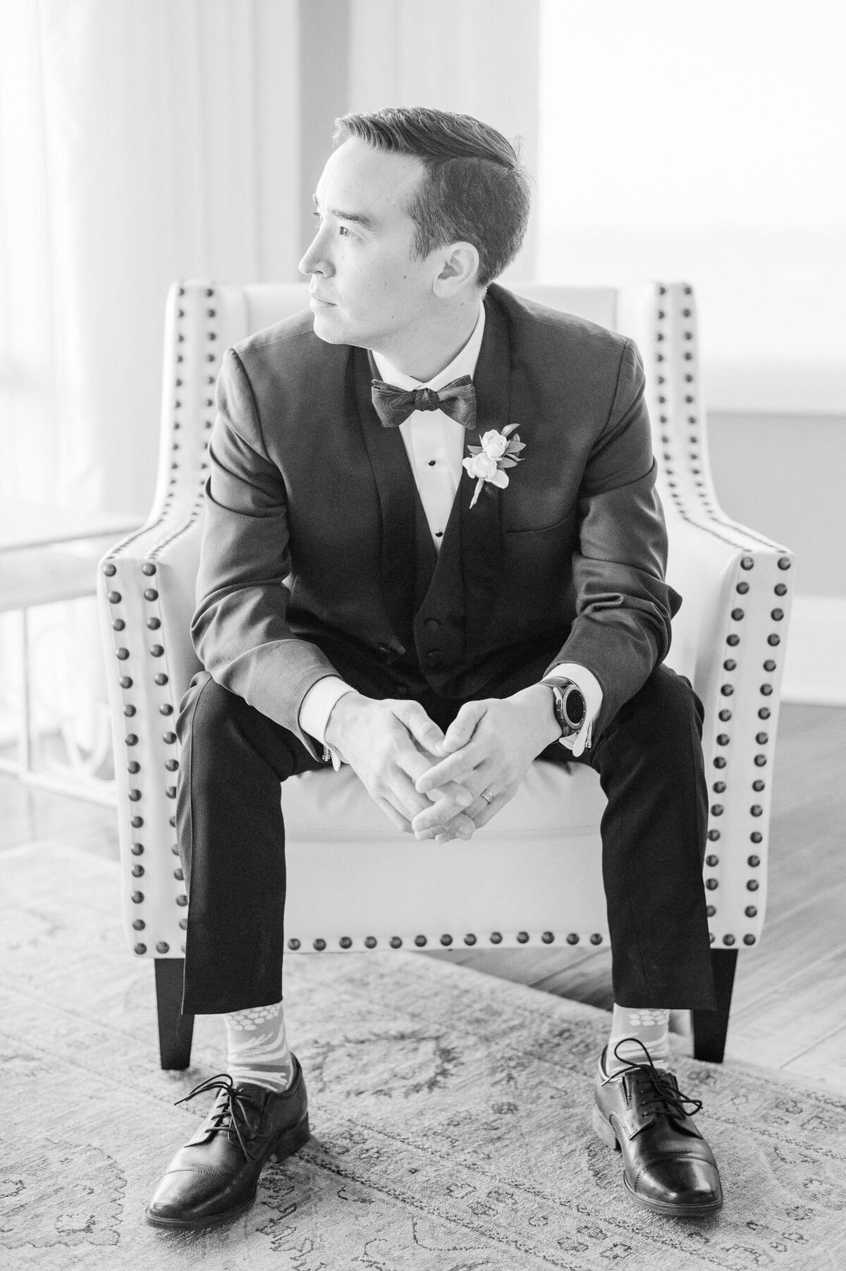 Groom sitting in a chair looking out the window in the bridal suite of the Pinery at the Hill.
