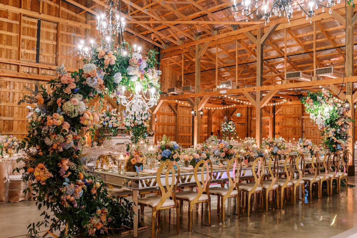 Head table with floral arches and hanging chandeliers with mirrored tables and floral centerpieces.