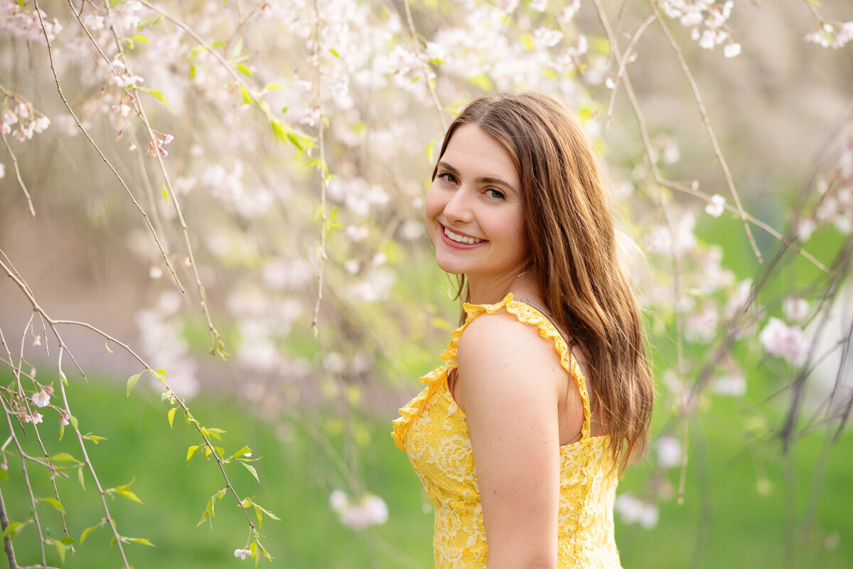 Senior session of young woman in yellow dress standing near flowers