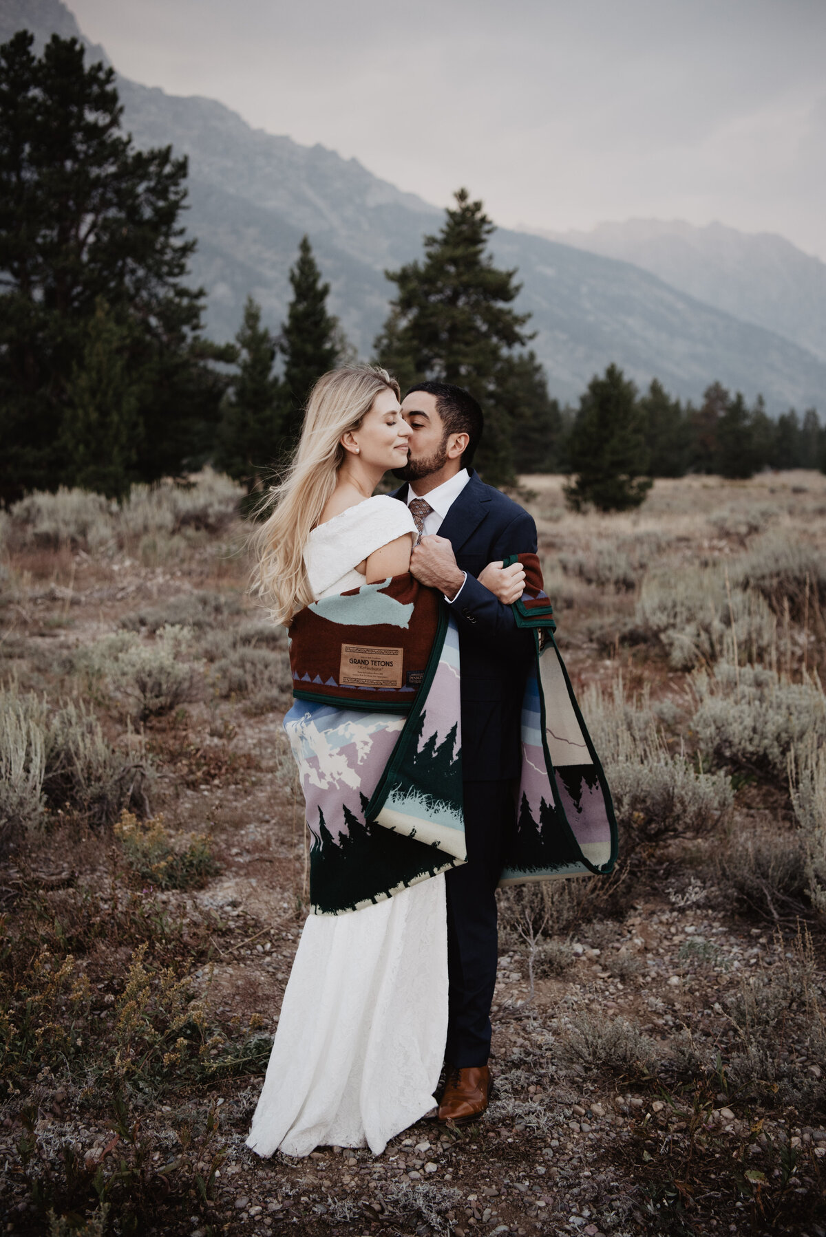 Photographers Jackson Hole capture bride and groom kissing in blanket