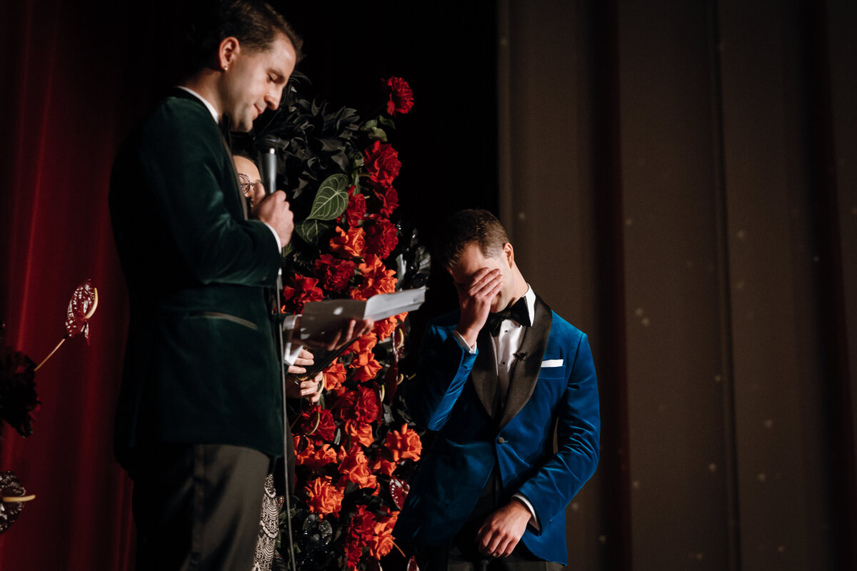 Groom saying his vows and his partner covering his face, crying.