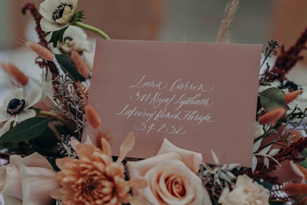 pink envelope with white ink calligraphy tucked into a  wedding bouquet