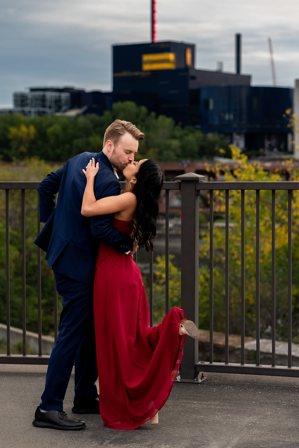 Man in blue suit and woman in red dress kiss in front of the Minneapolis skyline.