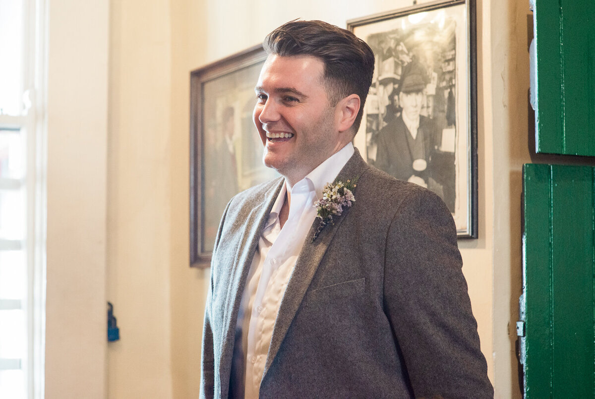 Wedding groom wearing buttonhole, standing in pub laughing