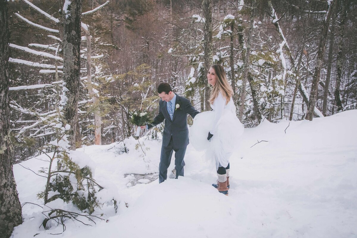 Bride laughs while hiking downhill in snow.