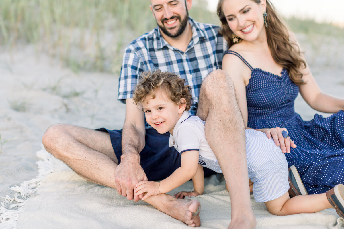 Son crawls on beach while mother and father watch by Karen Schanely Photography