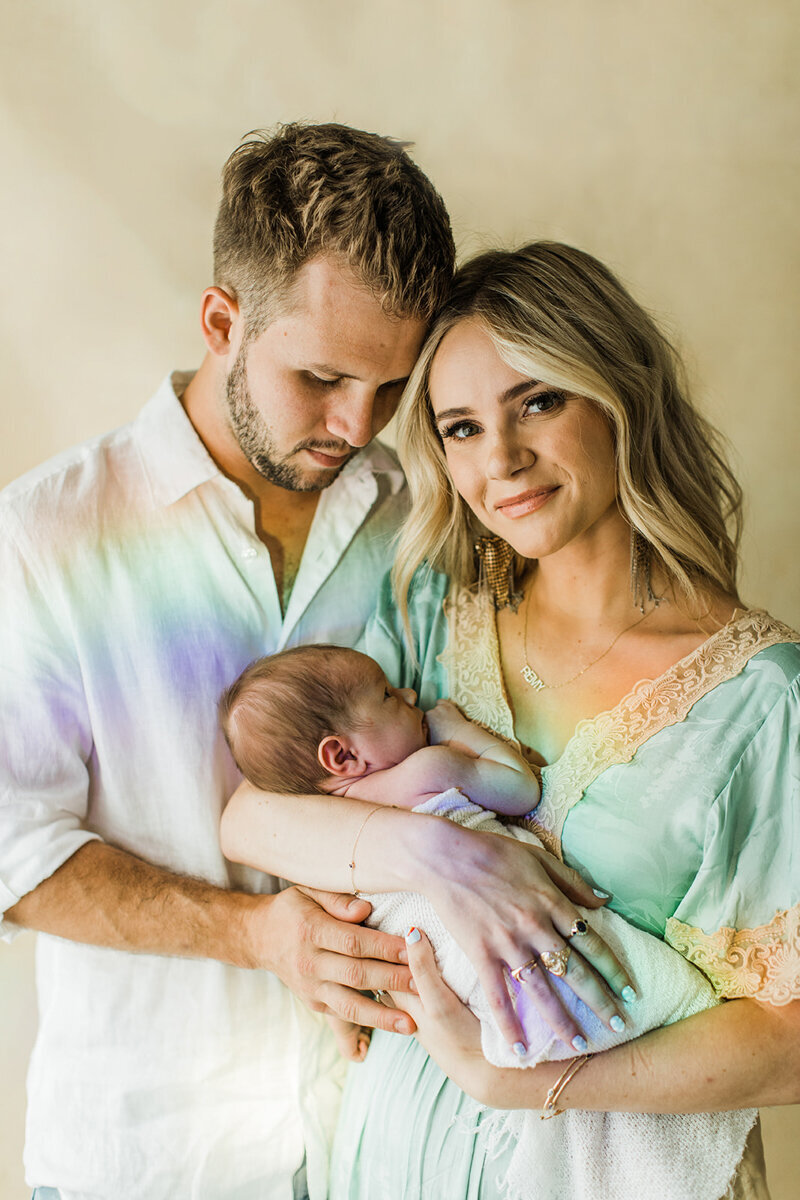 parents hold their newborn rainbow baby with rainbow projected onto them