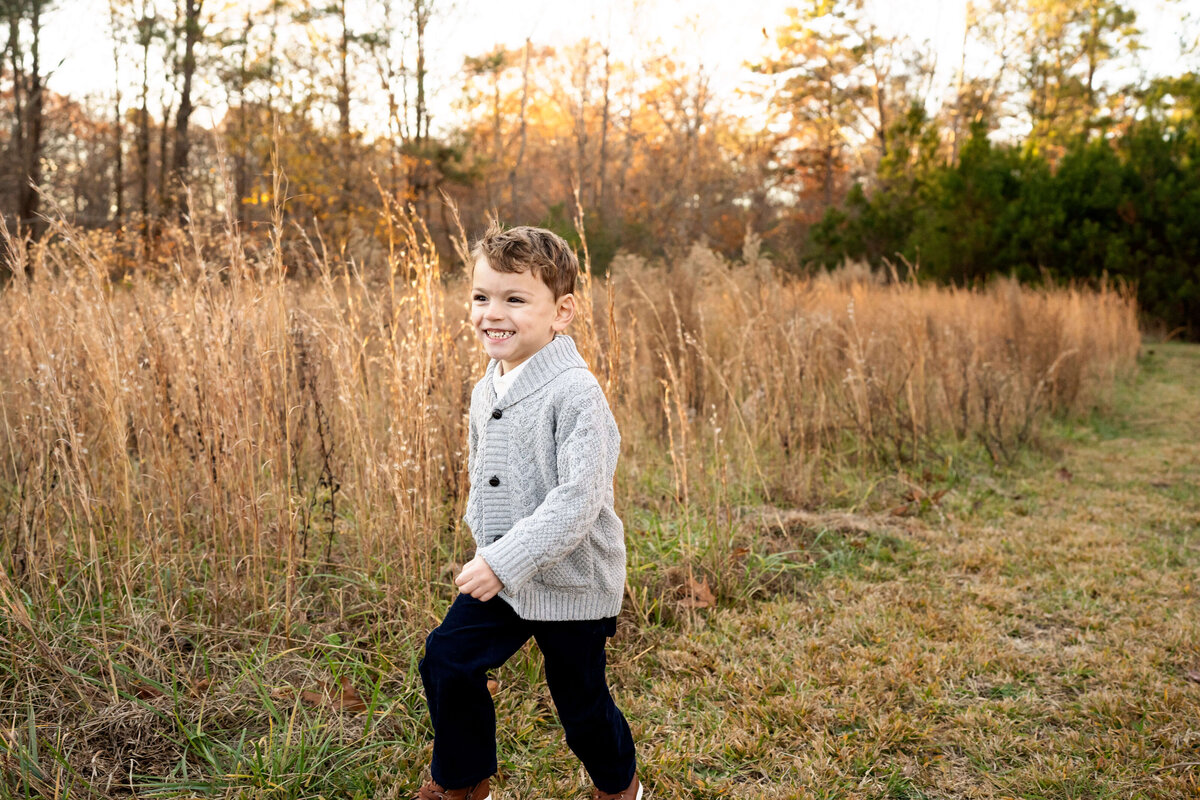 Young boy running through field of tall grass while smiling