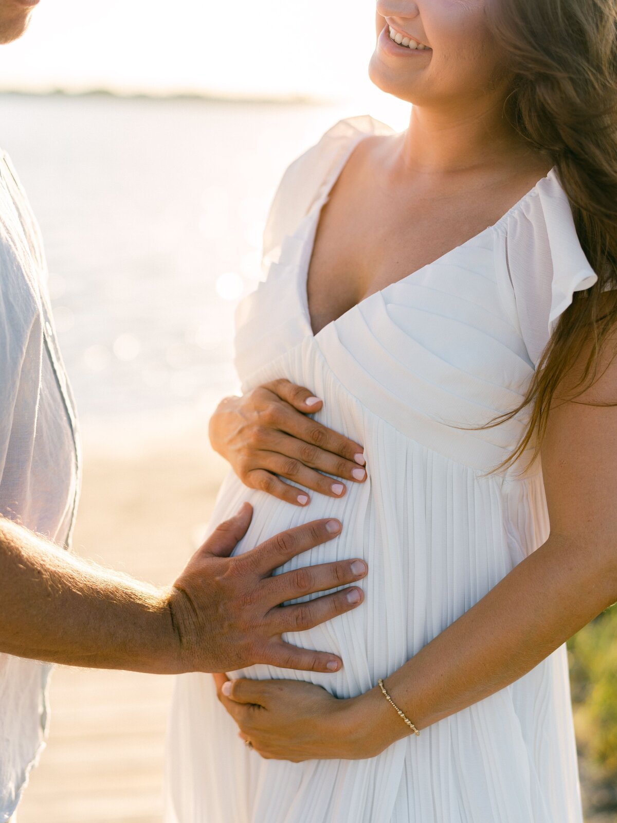 Couple placing hands on mother's pregnancy bump at the beach