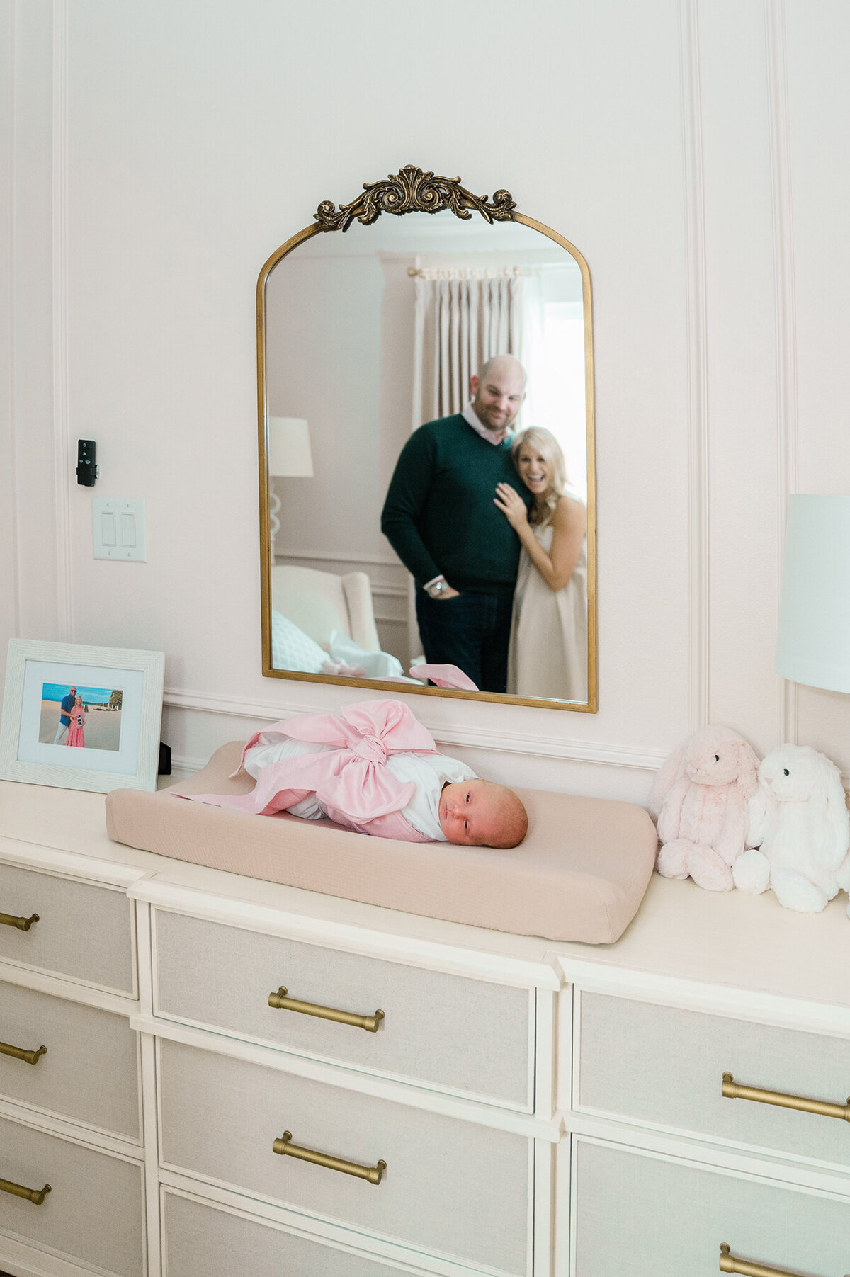 Newborn laying on a changing pad in a luxury Dallas nursery with a mirror above it reflecting her parents smiling at their baby.