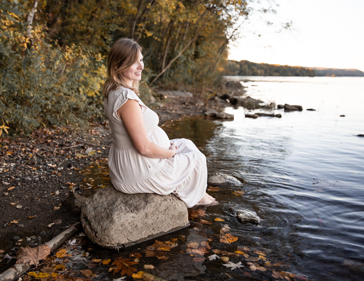 A mother poses for the photographer on a rock in the river during her maternity photos.