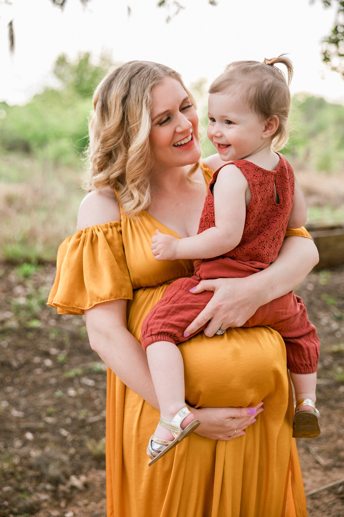 mom holds her daughter on top of her baby bump, wearing neutral earth toned dresses.