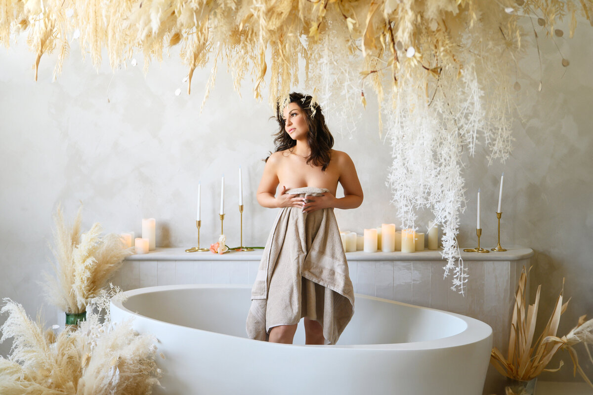 Brown-haired woman holding towel standing in a tub for her Toronto boudoir photography session.