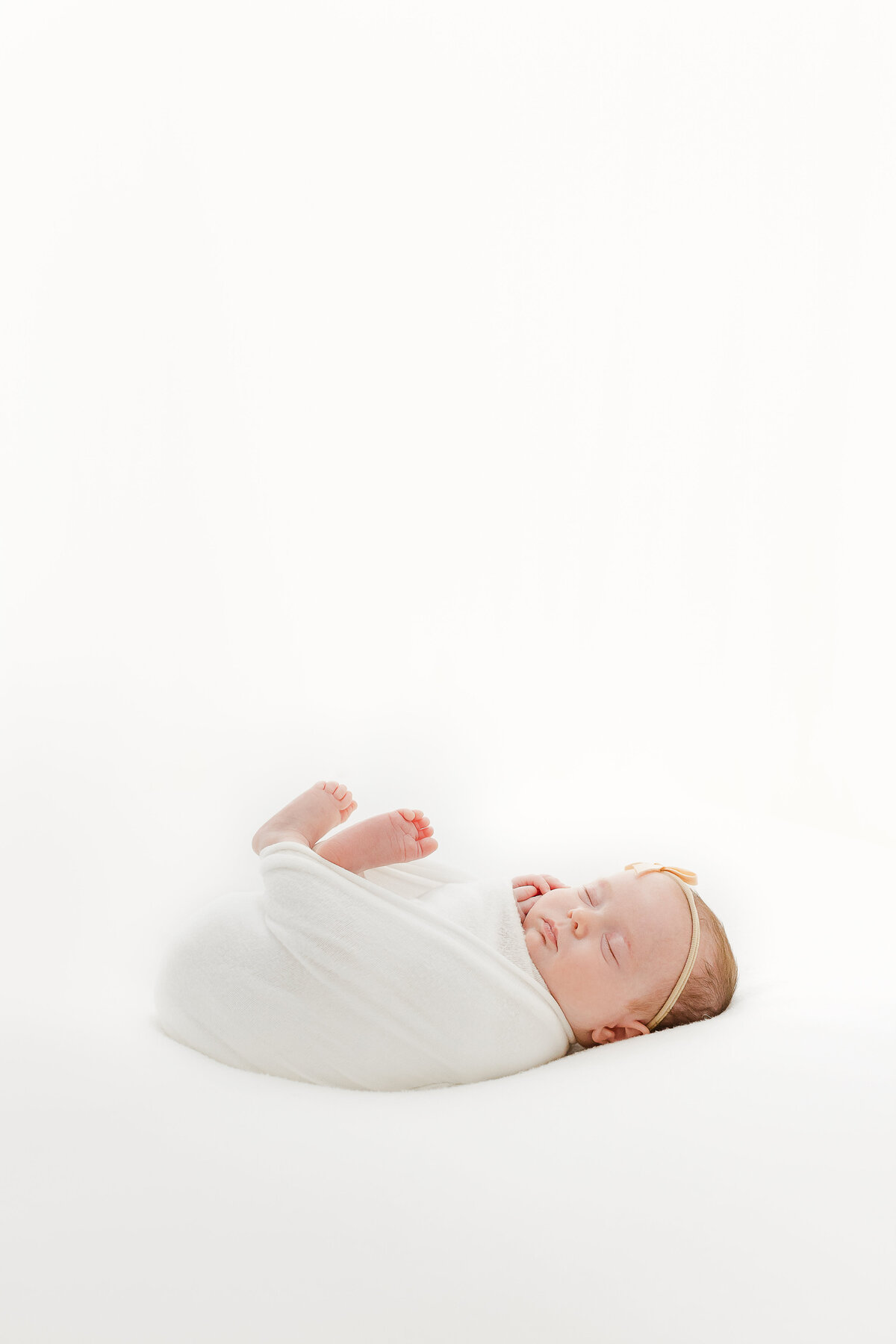 A DC newborn photography photo of a swaddled newborn baby girl in a white blanket with her feet sticking out