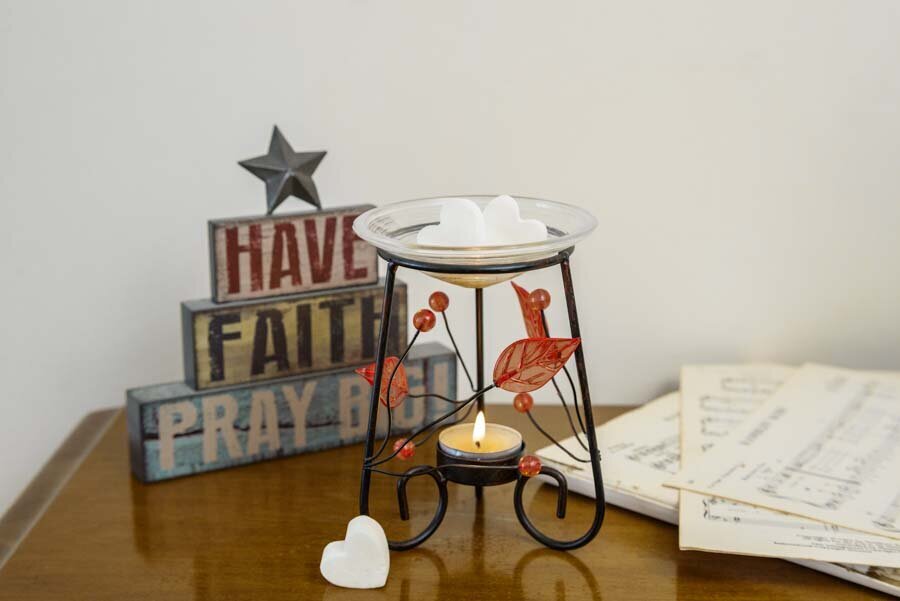 A candle holder with a lit candle on a wooden table, near decorative blocks saying "have faith pray big" and sheet music.