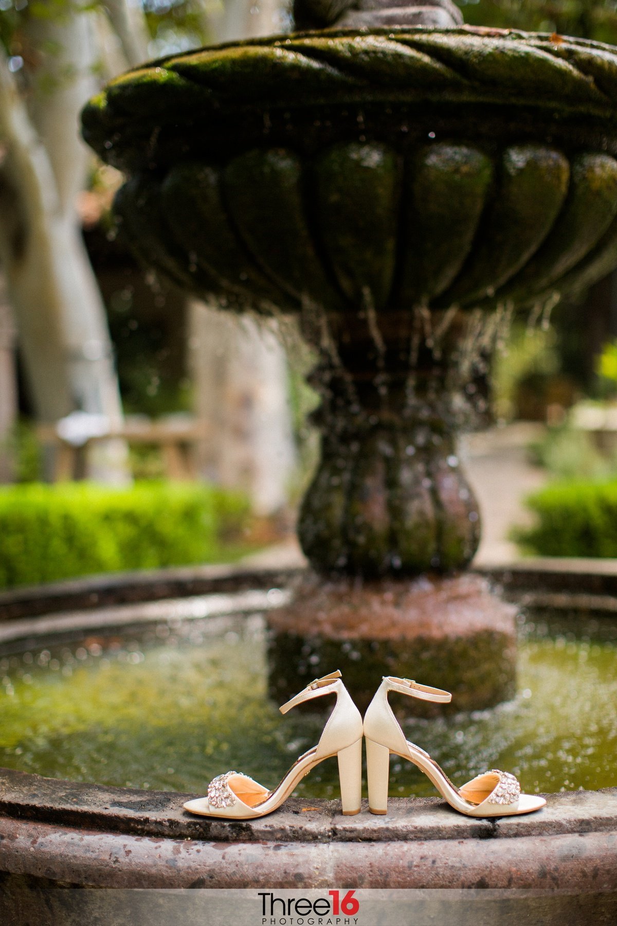 Bride's wedding shoes sit back to back on the edge of a water fountain