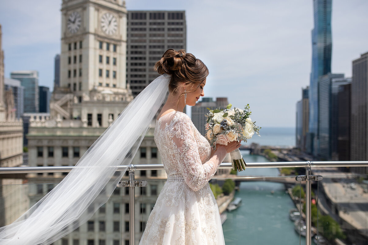 Bride in white wedding dress holding bouquet of flowers on top of the roof  in  Chicago Trump Tower