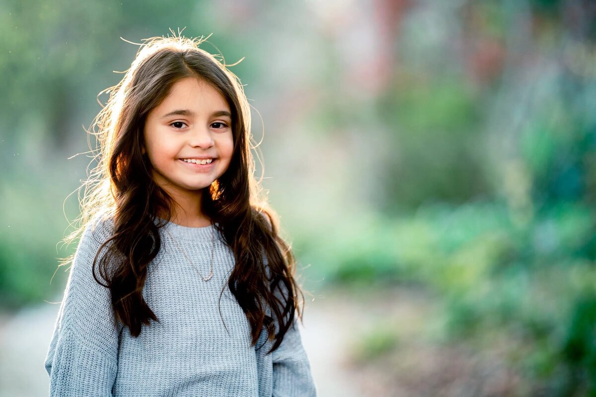 A small girl smiling while standing on a park path.