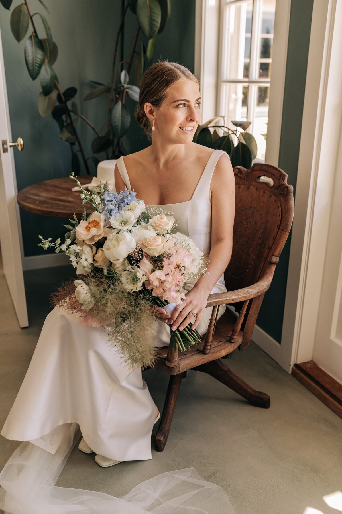 bride sitting in wooden chair green walls pastel flowers emilia wickstead wedding dress blenheim nz