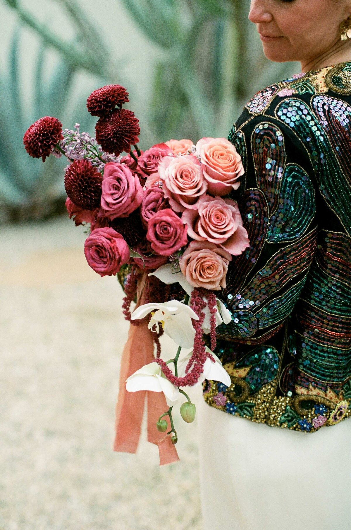 Bride wearing a colorful sequined jacket holding her mauve and purple bouquet