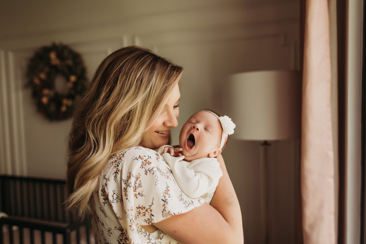 newborn baby girl yawns in moms arms in nursery