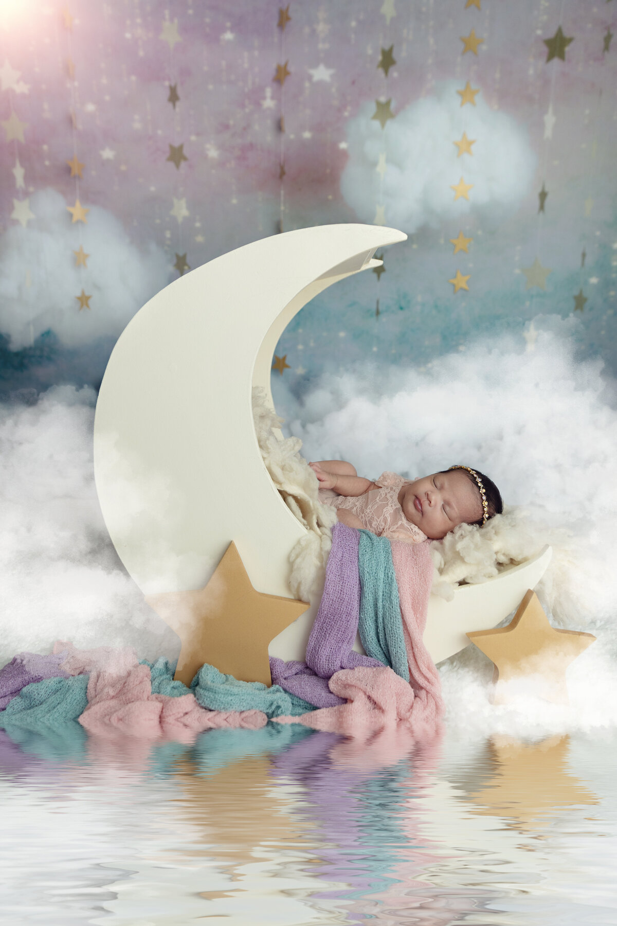 A newborn baby sleeps in a moon shaped crib with colorful blankets flowing out of it