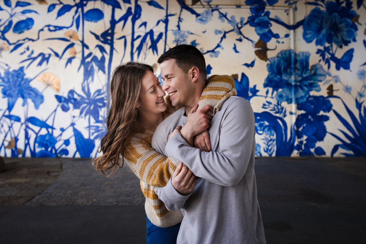 A couple holds each other in front of a blue and white mural in Chicago