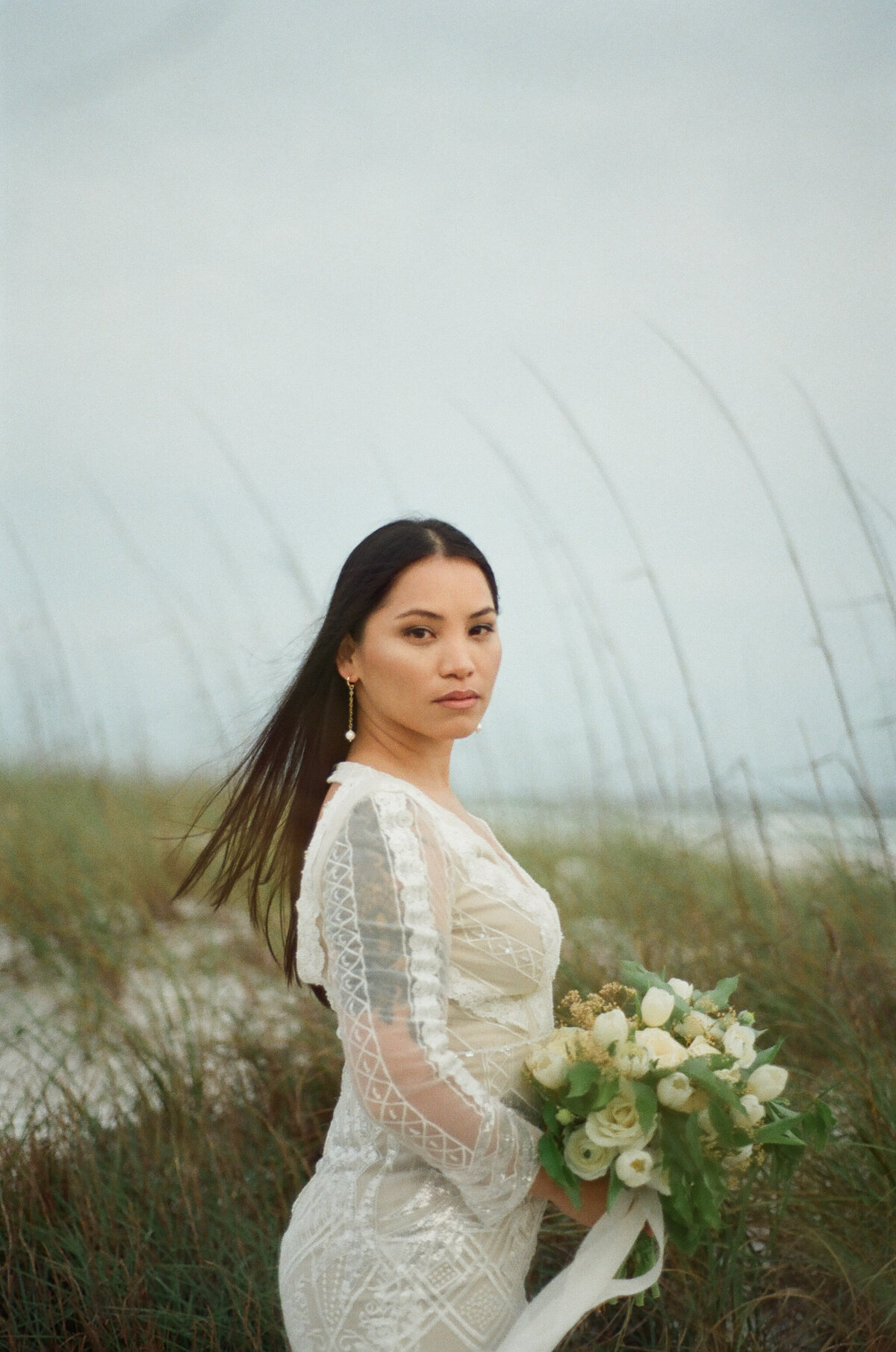 side shot of asian bride in bridal dress and veil walks on beach path - taken by panama city fl photographer Brittney Stanley