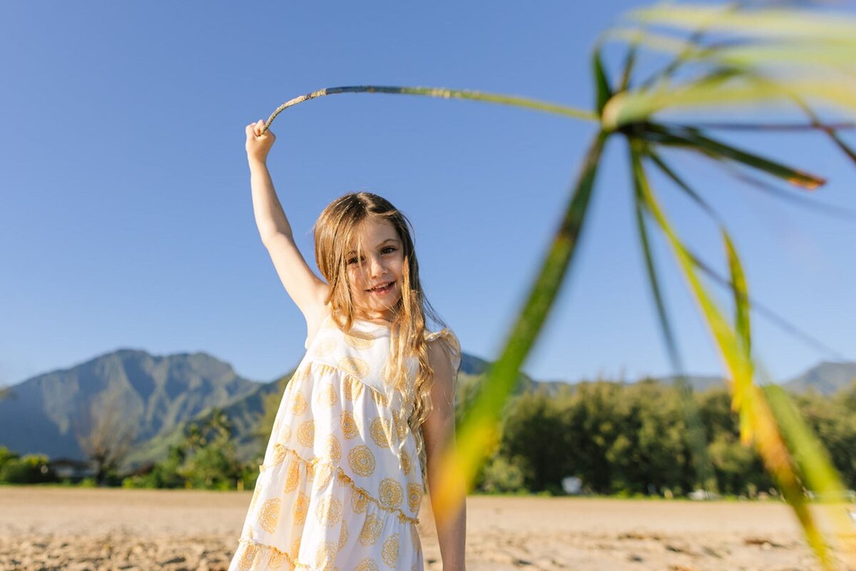 A little girl holds up a palm leaf, waving it in the air.