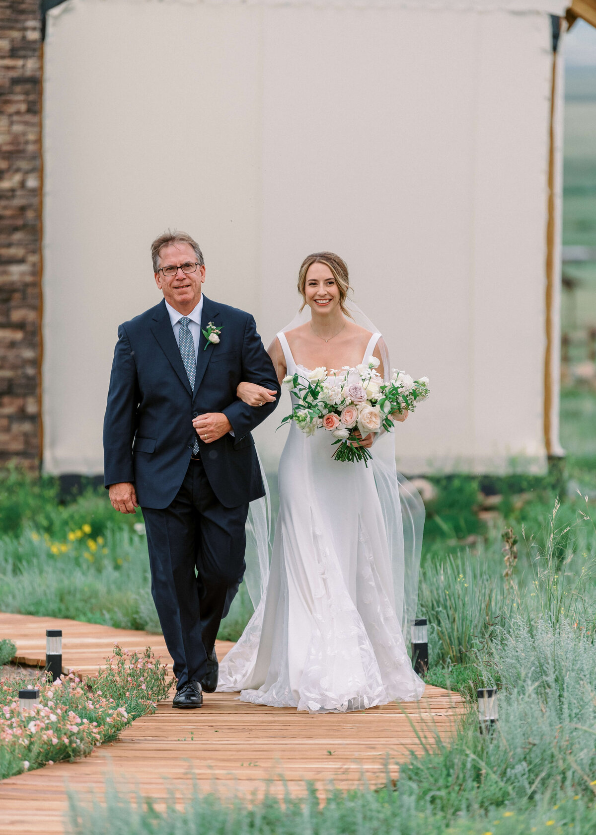 A proud father walks his daughter down the long walkway to her wedding ceremony