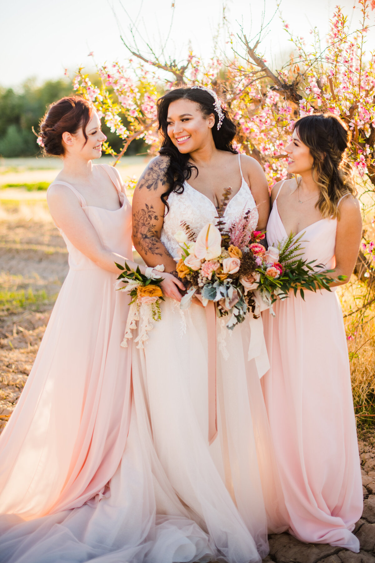 Bride with bridesmaids light pink dresses and bouquets smiling at each other cherry blossoms Schnepf Farms Meadows