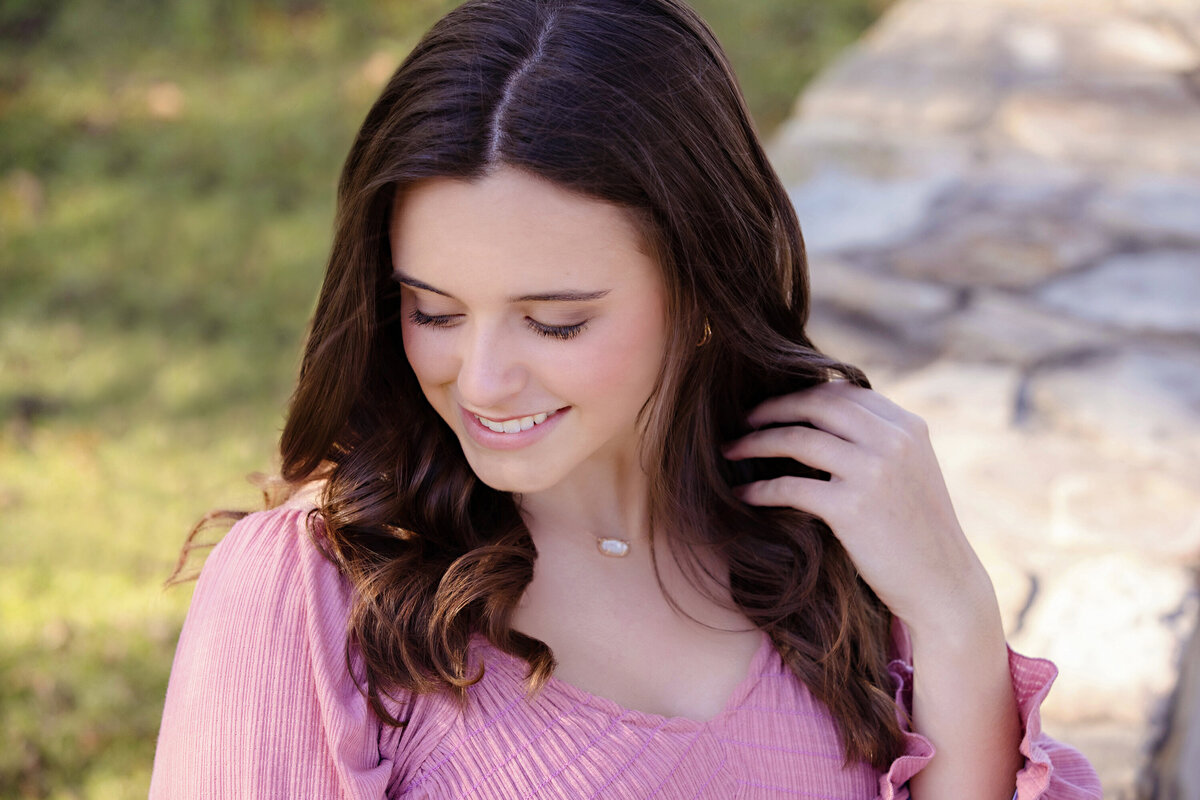 Radiant high school senior in pink v‑neck blouse smiling softly in golden afternoon light at Anne Springs Close Greenway