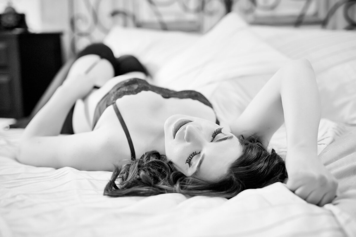 Black & White boudoir image of a woman in lingerie lying on a bed