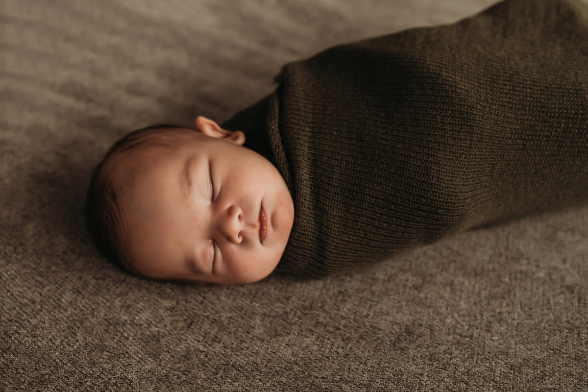 newborn baby bow wrapped in green blanket at home newborn session