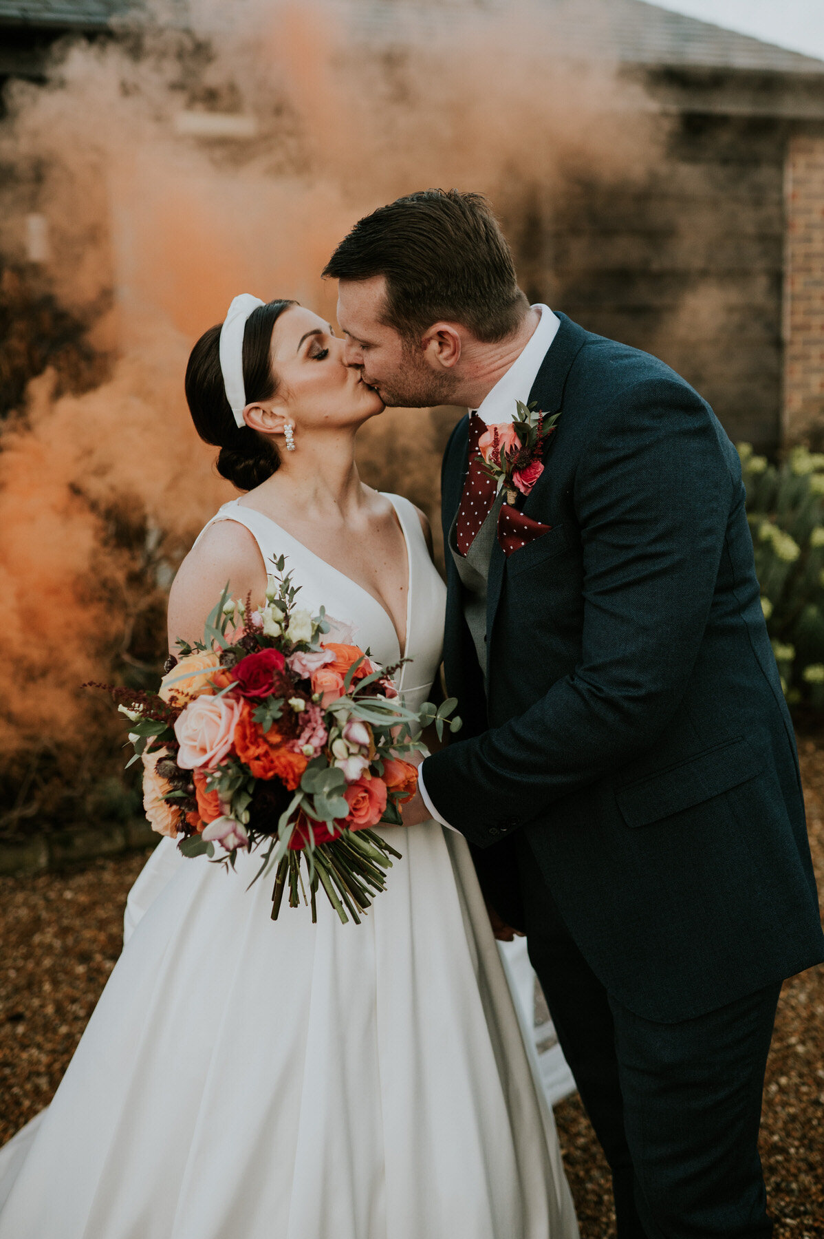 bride and groom kissing with an orange smoke bomb behind them