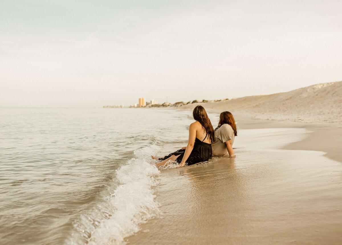 newly engaged lesbian couple sits on panama city beach at sunrise