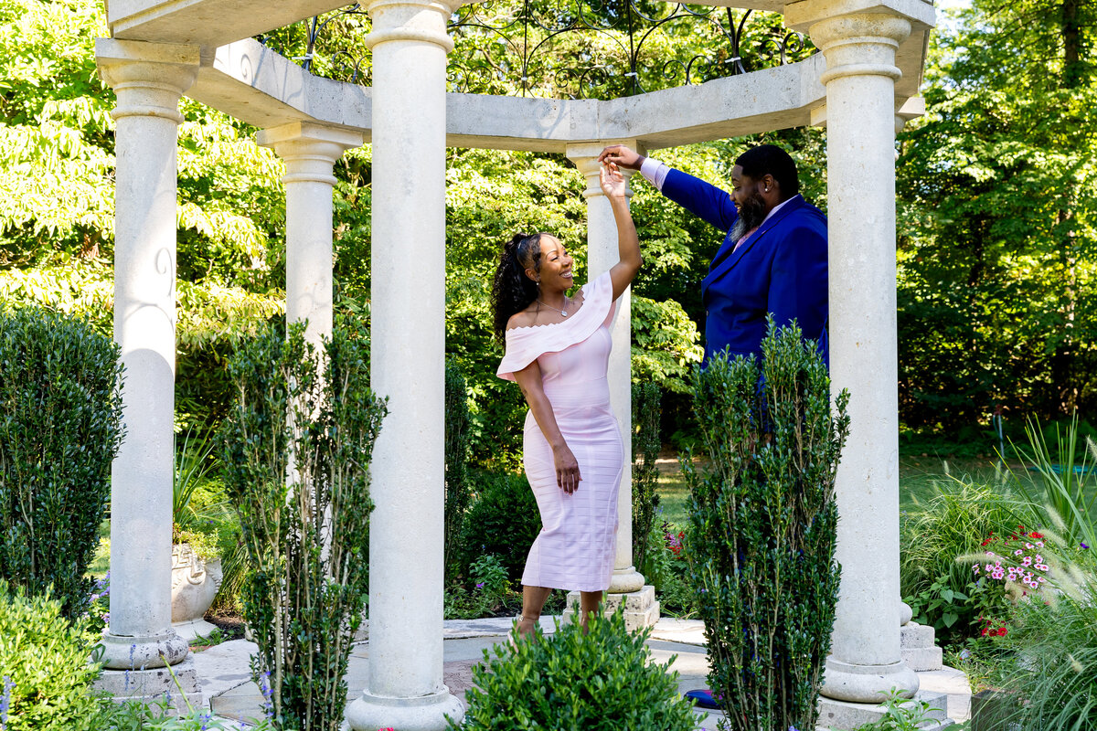 The young black couple is dancing in a garden for their engagements pictures. The day is sunny and clear skies.