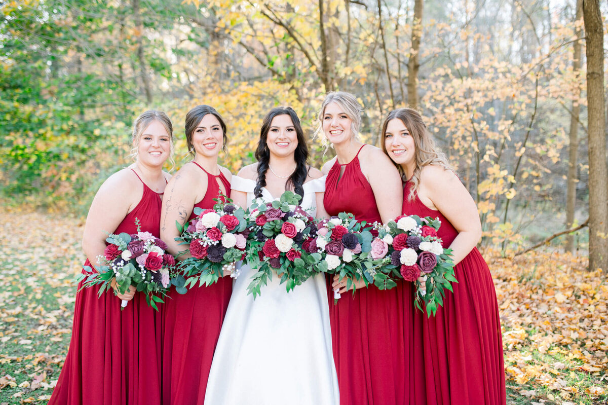 Bridesmaids holding flowers with leaves on the ground in the Fall time