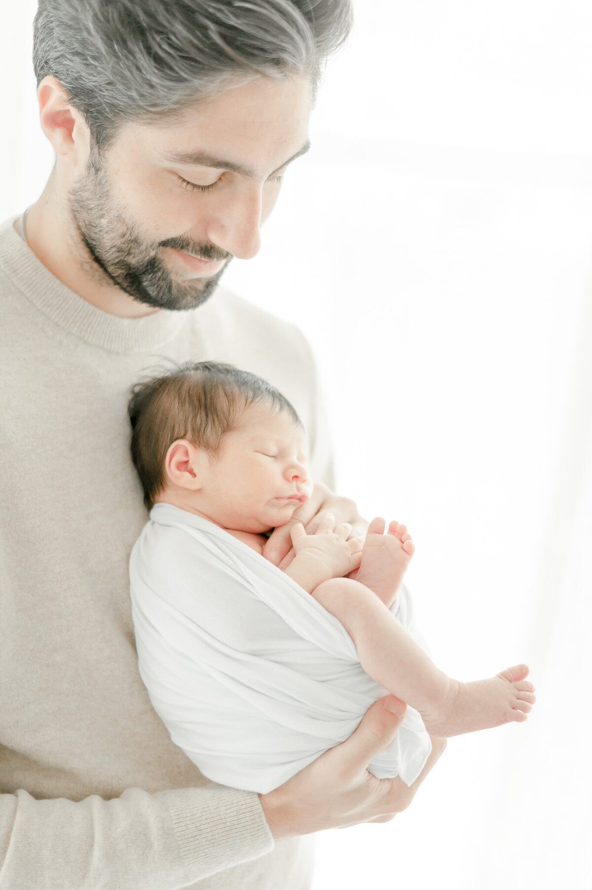father holds his sleeping baby near a window In Kristie Lloyd’s Nashville newborn photographer studio