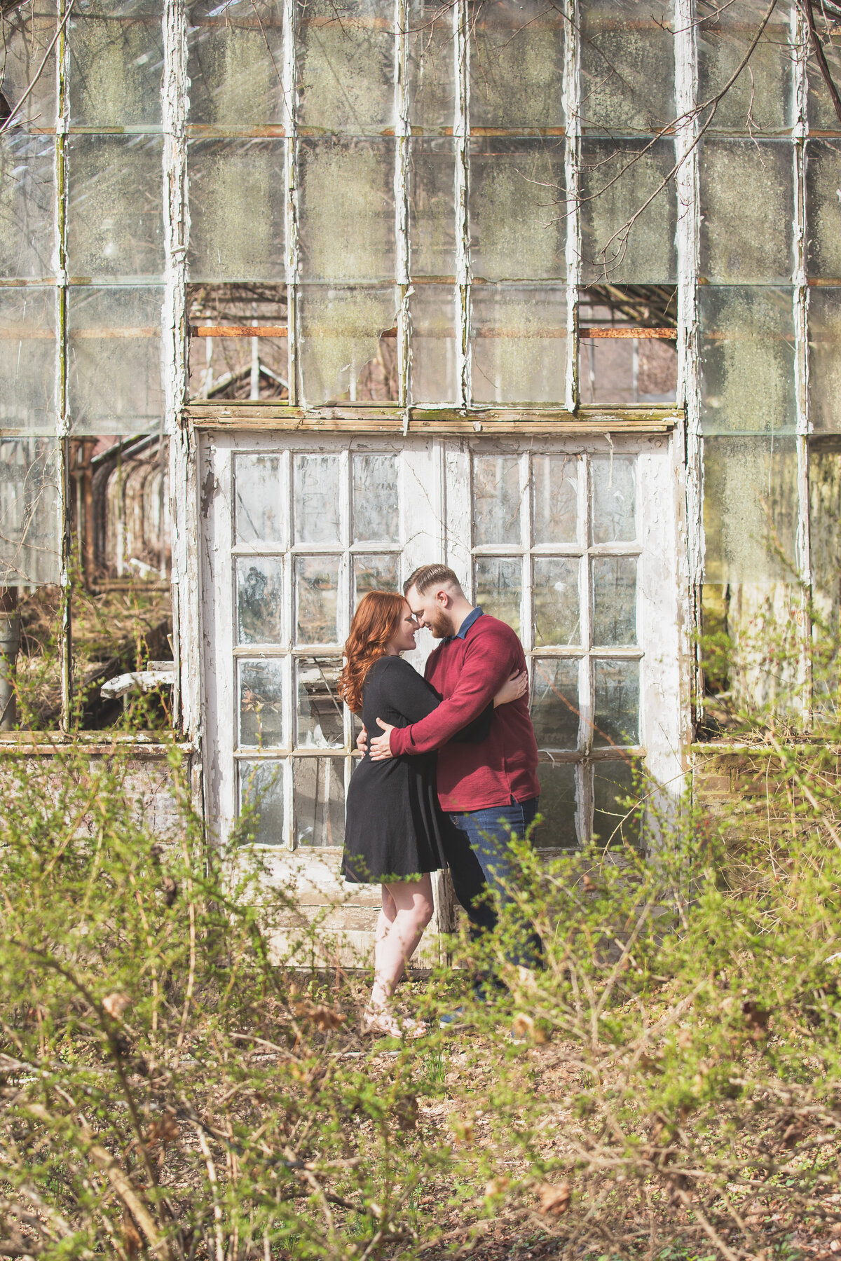 Engaged couple standing by old greenhouse