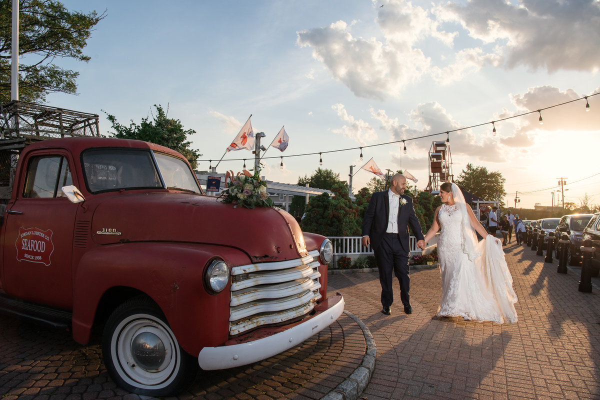 wedding photo of bride and groom holding hands and walking near red truck at The Loft by Bridgeview
