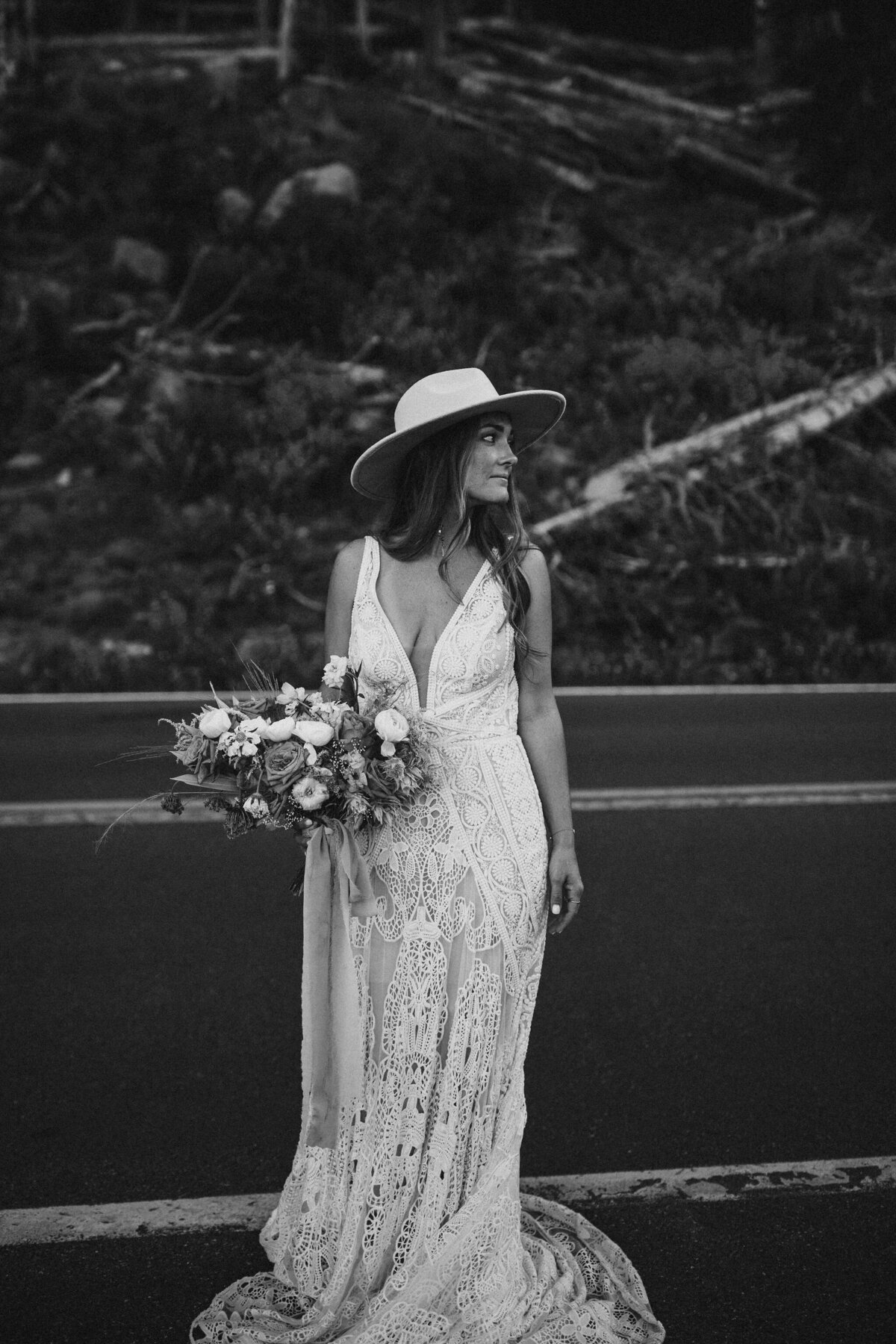 bride poses wearing a wedding gown and a hat holding a bouquet in the mountains